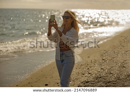 Carefree woman taking pictures of sunset using smartphone, standing by the sea