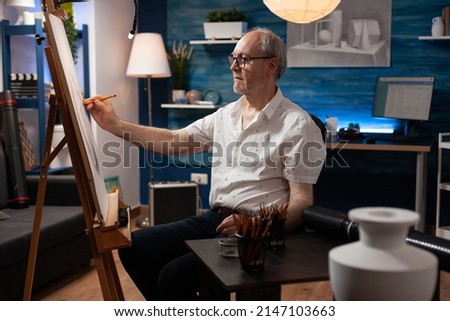 Senior art teacher sketching feeling inspired sketching vase on paper canvas using sharp pencil in home studio. Portrait of retired talented elederly man doing creative masterpiece on easel. Royalty-Free Stock Photo #2147103663