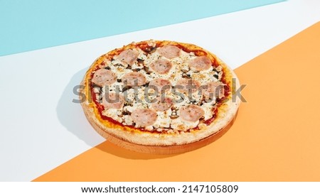 Italian pizza with ham and mushrooms on coloured background. Ham pizza in minimal style on orange and blue colours. American pizza delivery concept with color backdrop.