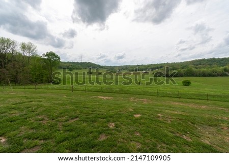 Farmland in Missouri USA, springtime green field grass and trees dark clouds moving under blue gray sky, country living at it best. Picture of home sweet home America. Horizontal Photo or Photograph,