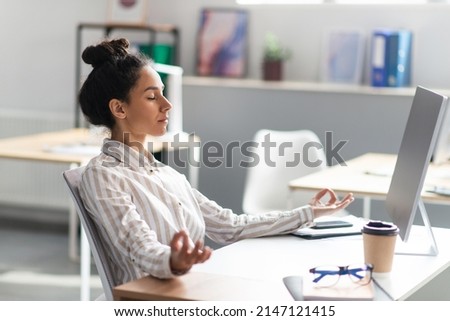 Coping with stress at work. Young latin office worker meditating at workplace in office after busy day, doing breathing exercises. Workplace stress management Royalty-Free Stock Photo #2147121415