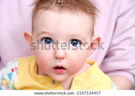Surprised infant baby boy with big blue eyes and disheveled hair in his mother arms. Portrait of a frightened child with a messy hairstyle