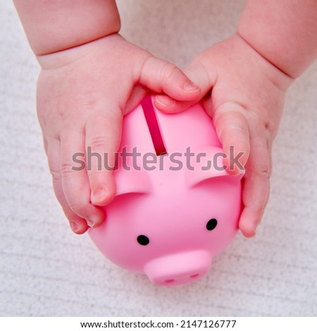 Baby hand and pink piggy bank, close-up. Children fingers and an object on a white background