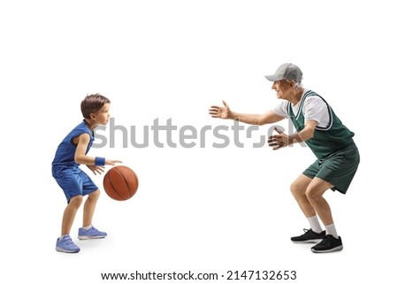 Full length profile shot of a boy and elderly man playing basketball isolated on white background