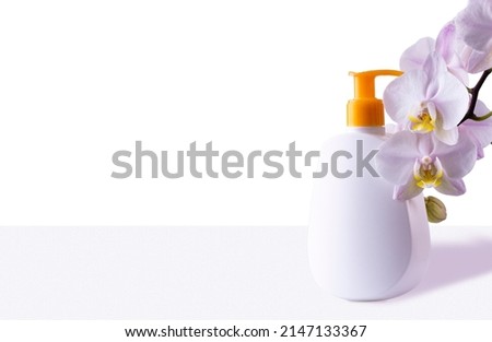 Bottle with hygiene or skin care product and branch with orchid flowers on blue background, space for text