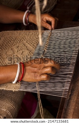 A village woman making jute door mat useing jute rope in a hand made machine. Royalty-Free Stock Photo #2147133681