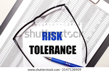 On a light background, a report, black-framed glasses, a pen and a sheet of paper with the text RISK TOLERANCE. Business concept
