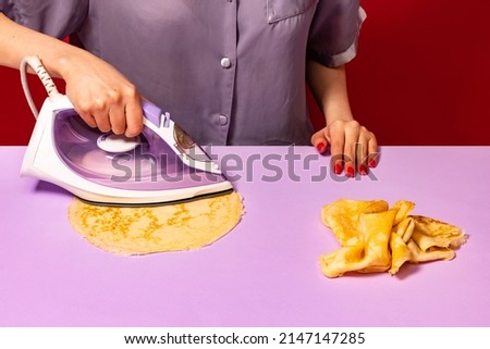 Pop art photography. Creative portrait of girl ironing pancakes on lilac color tablecloth. Vintage, retro 80s, 70s style. Complementary colors, Copy space for ad, text Royalty-Free Stock Photo #2147147285