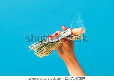 Rich and delicious fast food. Pop art photography.Female hand holding hot sausage wrapped in banknotes isolated on bright blue background. Vintage, retro style, surrealism, minimalism. Complementary Royalty-Free Stock Photo #2147147309