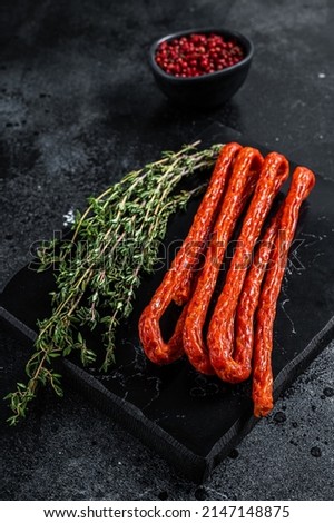 Smoked kabanos sausages with herbs on marble board. Black background. Top view.
