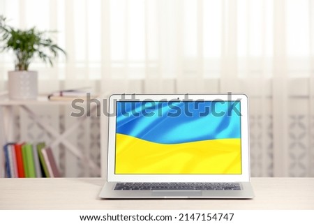 Modern laptop with picture of Ukrainian national flag on screen indoors