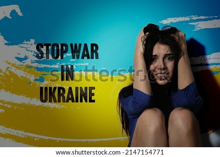Stop War in Ukraine. Afraid young woman sitting near wall painted in colors of Ukrainian national flag
