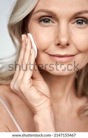 Pretty 50s middle aged old woman holding cotton pad sponge cleansing face skin purifying with cleanser, happy mature lady removing makeup enjoy healthy clean anti age dry skincare lifting routine. Royalty-Free Stock Photo #2147155467