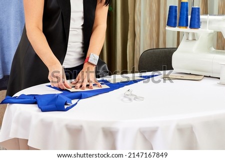 Female designer working with measure tape and sketches. Fashion tailor or sewer in a workshop  designing new clothes collection. Woman marking fabric in dressmaking salon.