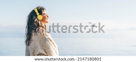 Young woman listening music with headphones on the beach in winter. 
