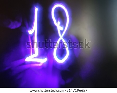 Glowing light purple number. On a dark glass matte background, the image of the number 18 is made by hand. The light of a laser pointer was used to create the inscription.