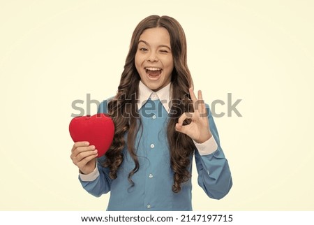 Playful girl hold red valentines heart showing OK hand gesture isolated on white, approval