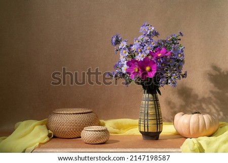 Summer purple flowers in a vase and a pumpkin on the table. Asters
