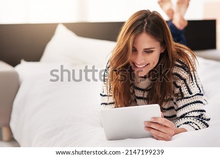 Unwinding online. Shot of a beautiful young woman using a digital tablet at home. Royalty-Free Stock Photo #2147199239