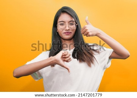 Young woman making good-bad sign. Undecided between yes or not on isolated orange background