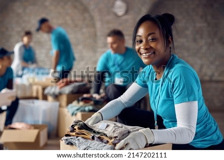 Happy African American woman volunteering at humanitarian aid center and looking at camera. Royalty-Free Stock Photo #2147202111