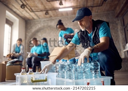 Mature man working as volunteer at community center and arranging donated food and water in boxes. Royalty-Free Stock Photo #2147202215