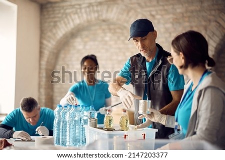 Food bank volunteers preparing donation boxes for people in need. Focus is on mature man.  Royalty-Free Stock Photo #2147203377