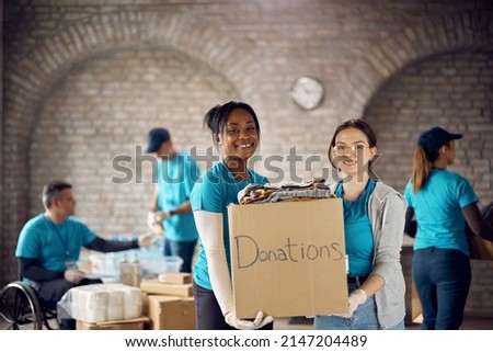 Young multiracial women working as volunteers and holding donation box while looking at camera.  Royalty-Free Stock Photo #2147204489