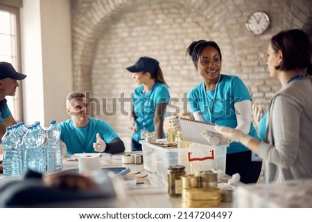 African American volunteer going through donation checklist while talking to her associate at food bank. Royalty-Free Stock Photo #2147204497