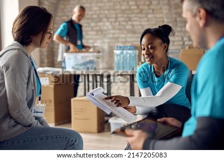 African American volunteer coordinator giving instructions to her coworkers while going through checklist at community center. Royalty-Free Stock Photo #2147205083