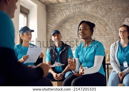 Team of volunteers having a meeting while working at donation center. Focus is on African American coordinator.  Royalty-Free Stock Photo #2147205101