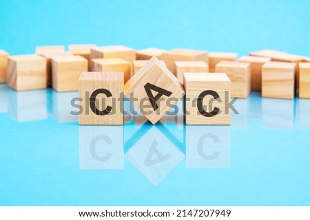 text CAC - written on the wooden cubes in black letters, the cubes are located on a bright blue glass surface. concept word forming with cubes on background. CAC - short for Customer Acquisition Cost