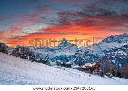 Beautiful view of snow covered houses in village. Majestic mountain range against cloudy sky during sunset. Holiday homes in alpine region during winter. Royalty-Free Stock Photo #2147208165