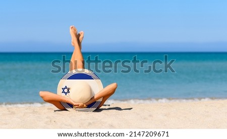 A slender girl on the beach in a straw hat in the colors of the Israel flag. The concept of a perfect vacation in a resort in the Israel. Focus on the hat. Royalty-Free Stock Photo #2147209671