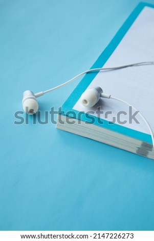 Top view of white headphones and notebooks on blue background with copy space. Flat lay. Audio book concept