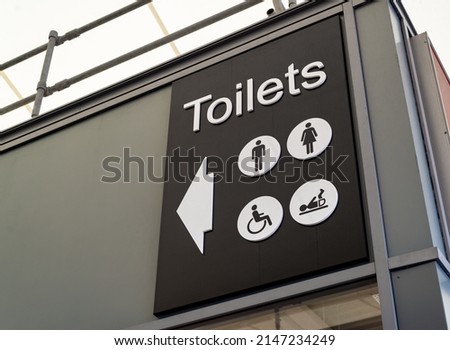 Large black and white toilets sign with men, ladies, disabled and baby changing icons and arrow pointing towards the restroom.