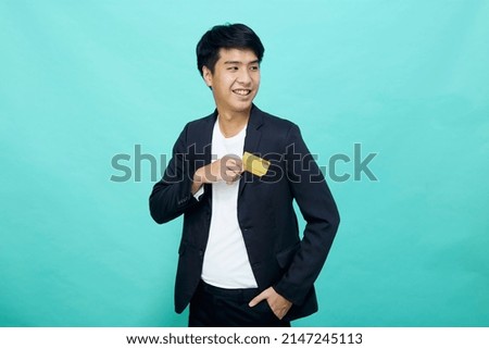 Portrait Young handsome businessman in a suit holding yellow credit card, isolated in a blue studio