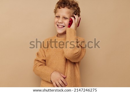 Cheerful boy talking on the phone on a beige background