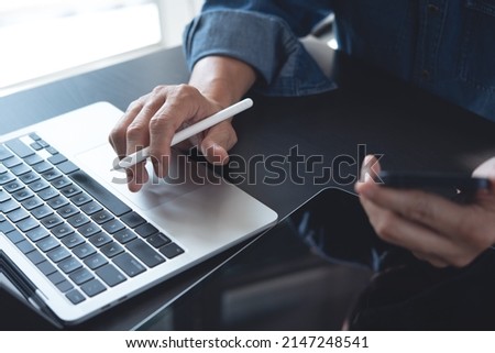 Business man working on laptop computer and using mobile phone, surfing the internet with digital tablet on office table. Man searching data via computer, online working, telecommuting concept