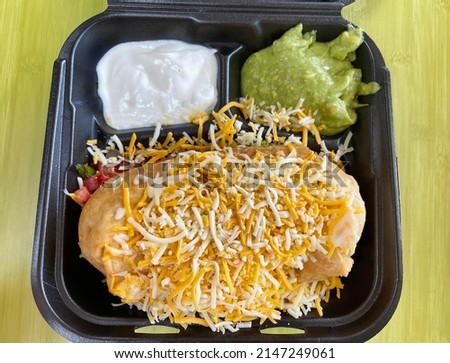 A chimichanga with toppings on the side in a black to go Styrofoam container.