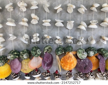 Many row seaside mobile or shell mobile are hanging on concrete wall. Tropical nature work art for house interior or souvenir from sea.