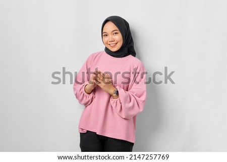Smiling young Asian woman in pink shirt holding hands together and feels optimistic isolated over white background