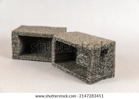 Minimalist geometric composition of pieces of black foam against a gray background. Two random pieces of material that is used to protect the seal of postage.