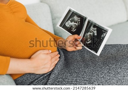Pregnant woman looking at first ultrasound photo of her baby, caressing her belly happily awaiting the birth of her child. First trimester pregnancy Royalty-Free Stock Photo #2147285639