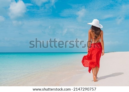 Luxury beach vacation elegant tourist woman walking relaxing in red beachwear and sunhat on white sand Caribbean beach. Lady tourist on holiday vacation resort Royalty-Free Stock Photo #2147290757