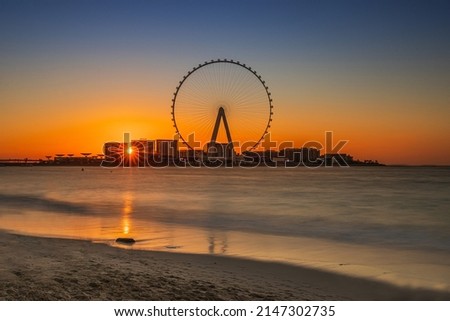 Dubai beach at sunset. Jumeirah Beach Residence with the world largest Ferris wheel. Sunbeams between the houses. Ain Dubai at sunset with a blue orange sky. Royalty-Free Stock Photo #2147302735