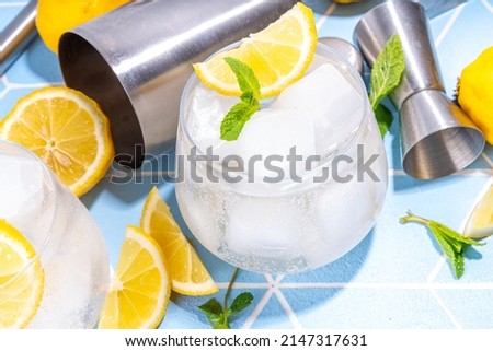 Cold lemon detox water, infused citrus sour sweet mocktail, lemonade cocktail with crushed iced, lemon slices on summer sun lighted blue tiled background copy space
