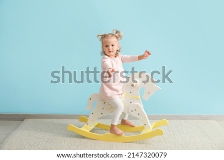 Adorable baby girl with rocking horse near blue wall Royalty-Free Stock Photo #2147320079