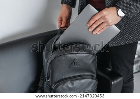 Man hand pulls a gray laptop with a black leather stylish backpack Royalty-Free Stock Photo #2147320453