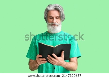 Senior man reading Holy Bible on green background